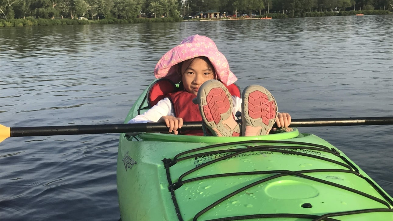 A young girl takes a break from paddling in a kayak.