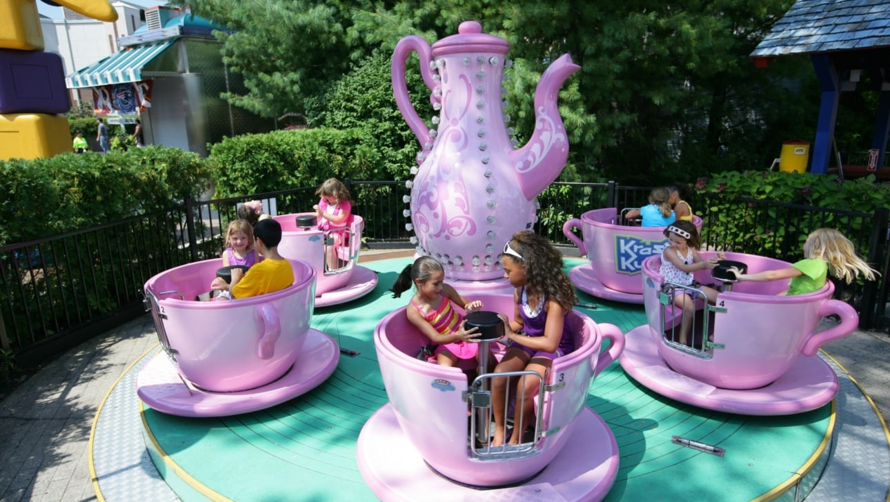 Children ride in spinning teacups at an amusement park.