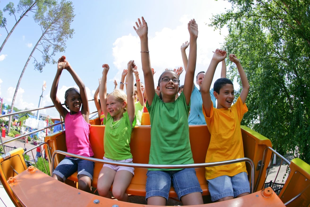 Kids riding a roller coaster with their hands in the air at an amusement park.