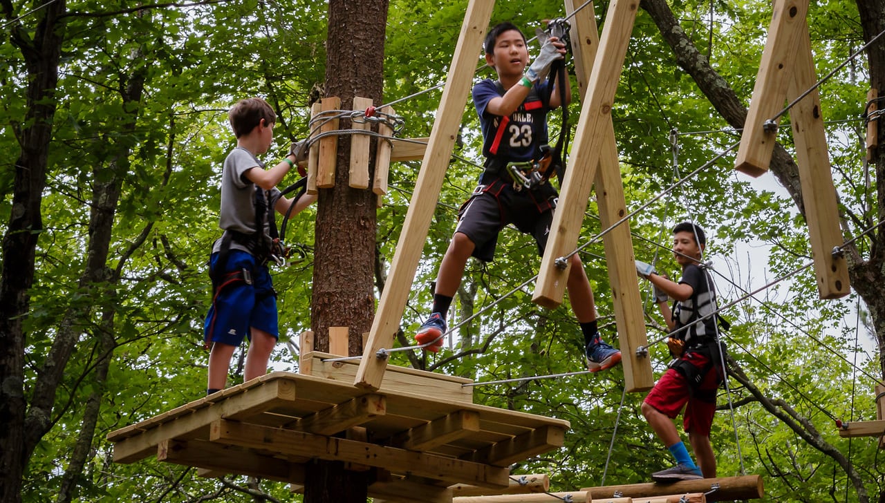 Three boys navigate a high ropes element on a challenge course.