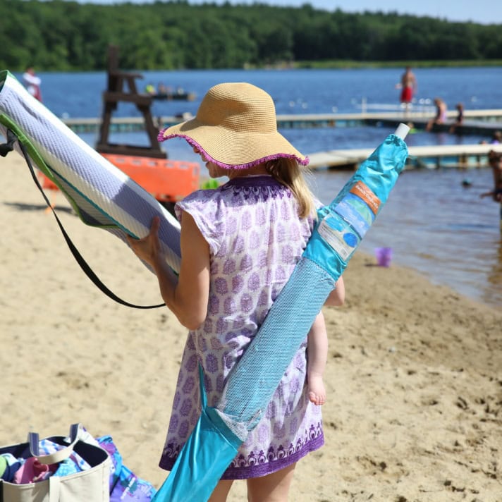 A woman with an umbrella and chair looks for a spot on the beach