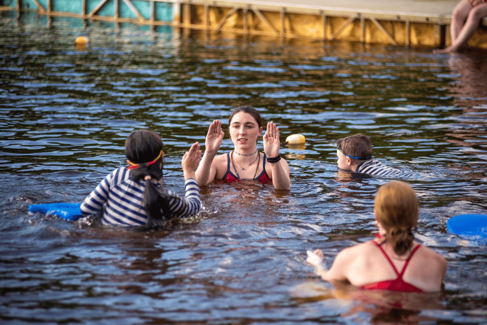 Children taking swimming lessons with instructors in a lake