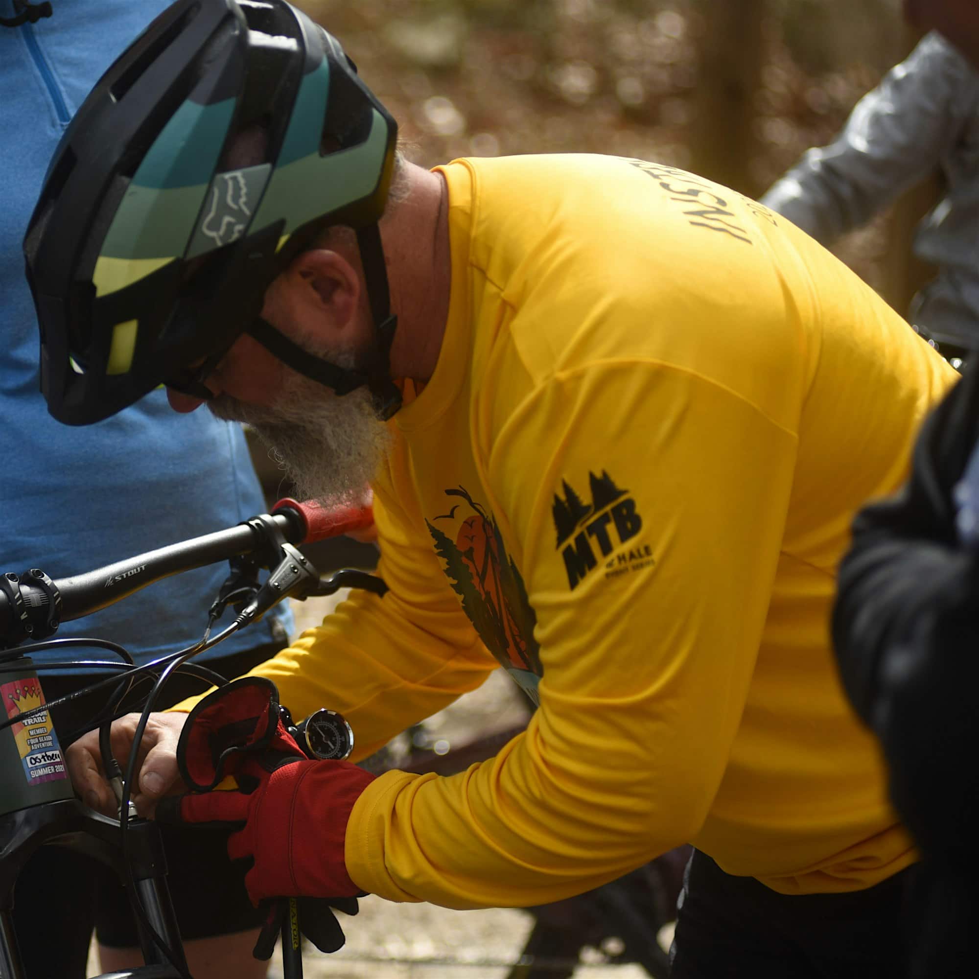 A person in a yellow long-sleeve shirt and helmet works on a bicycle outdoors.