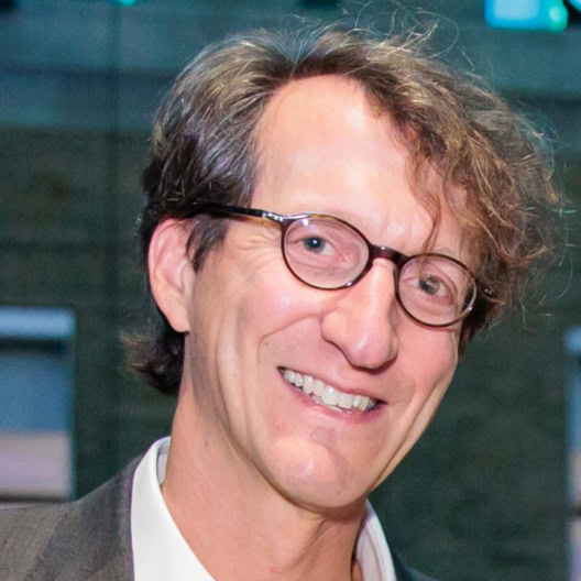 Dan Frankel, wearing glasses and smiling, in a white dress shirt and dark jacket.
