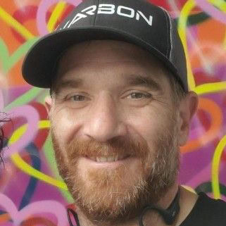 Man with a beard wearing a cap stands in front of a colorful, abstract background.