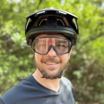Wes Jacobsz wearing a black bike helmet and protective eyewear smiles outdoors against a leafy background.