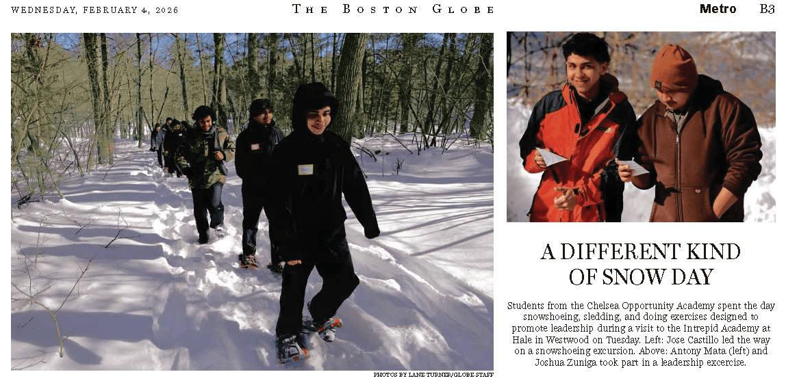 A group of students walks in single file through a snowy forest, wearing snowshoes, as part of an outdoor learning activity.