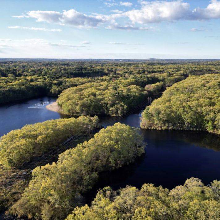 Aerial view of a winding river surrounded by dense green forest under a partly cloudy sky.
